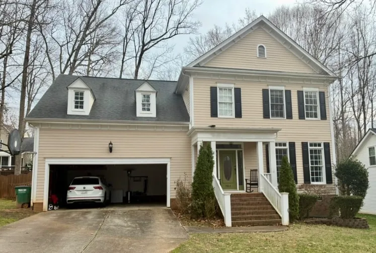 Two story colonial home in dated tan siding with dark shutters before repainting