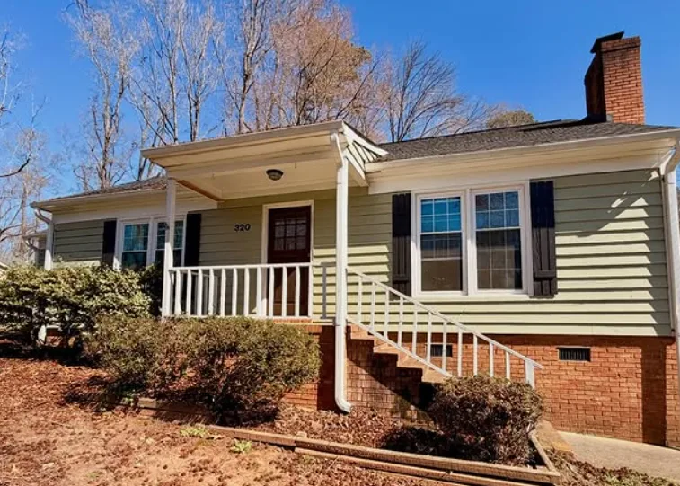 Single story ranch home in faded sage green siding with black shutters before repainting